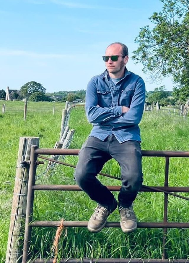 Luke from CIS Books sitting on a field gate in the Cotswolds